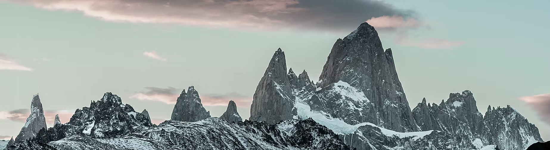 Chaîne de montagnes rocheuses enneigée sous un ciel nuageux au crépuscule.