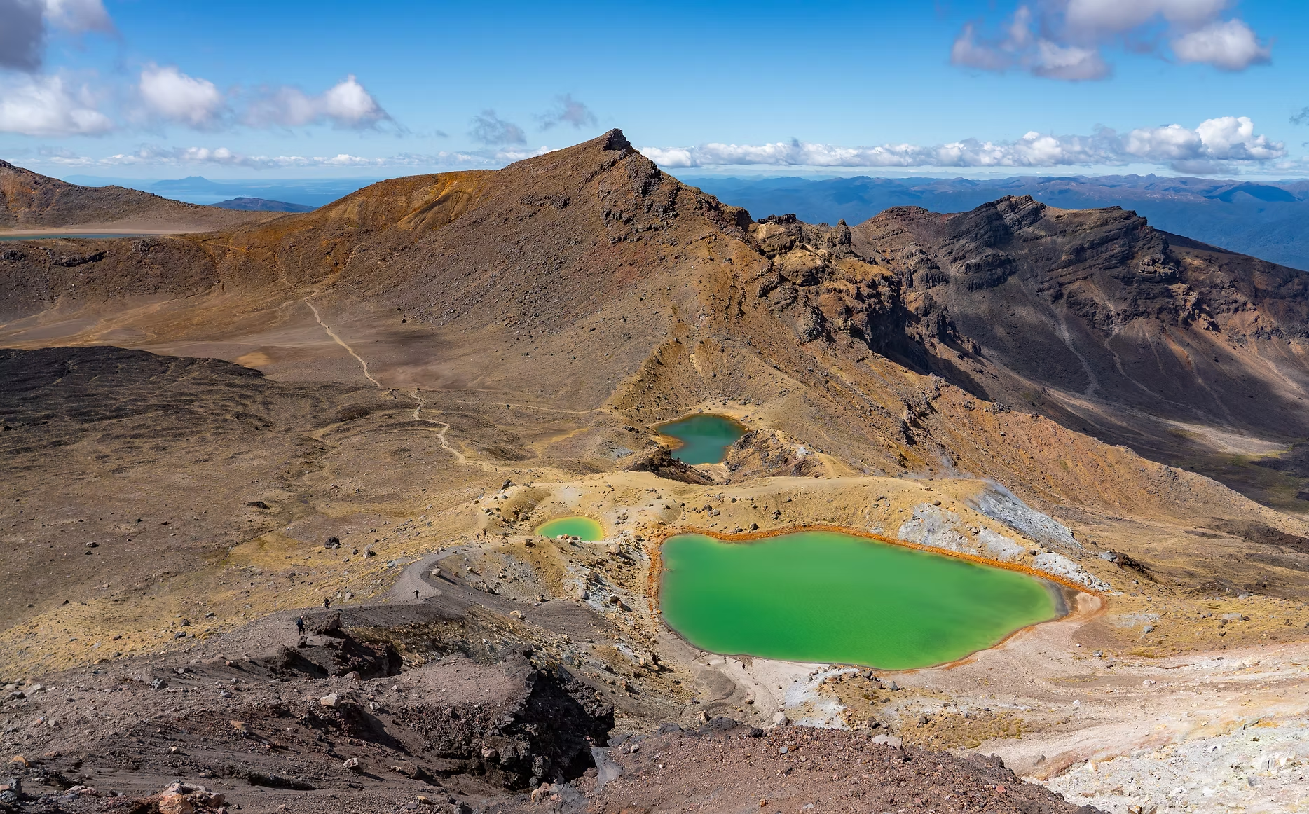 Vue panoramique de cratères volcaniques avec deux lacs verts, un paysage rocheux et montagneux sous un ciel partiellement nuageux.