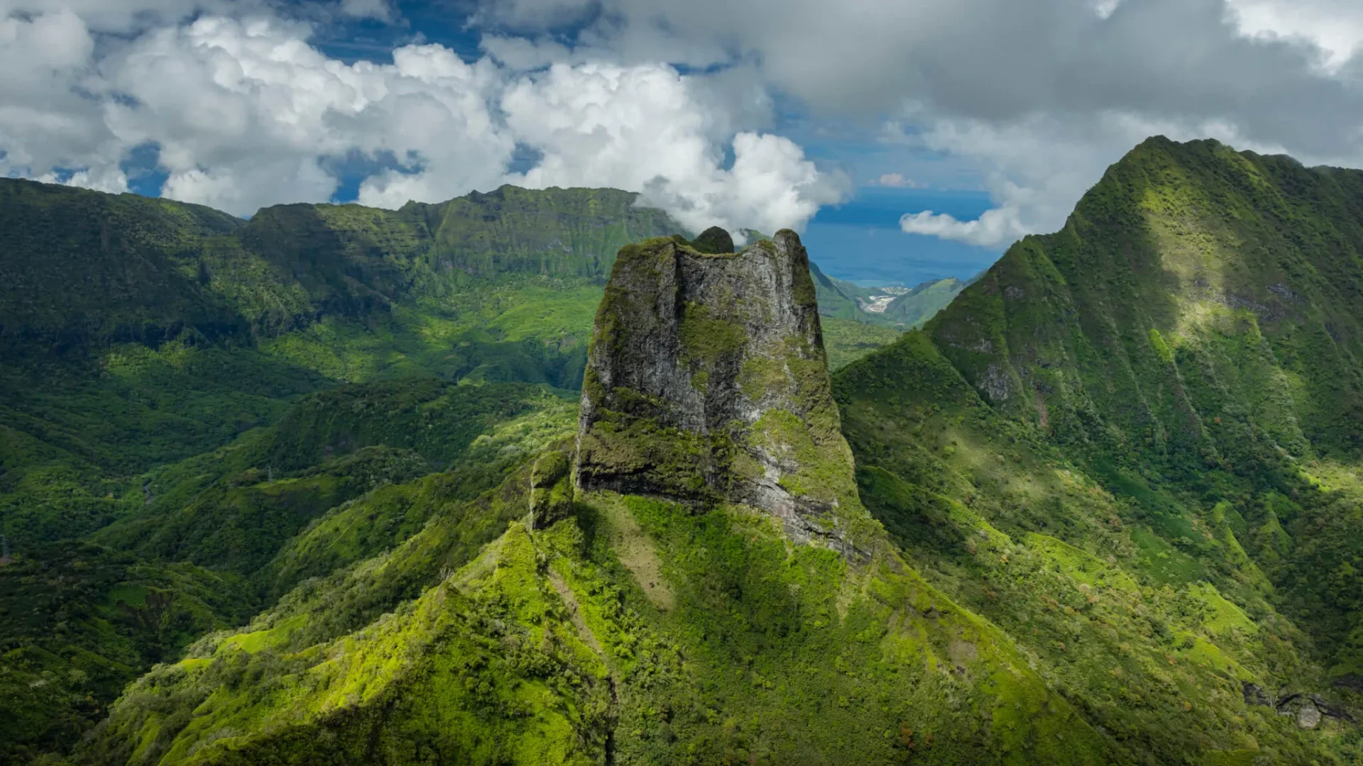 Paysage de montagnes verdoyantes avec une formation rocheuse au centre, sous un ciel nuageux.