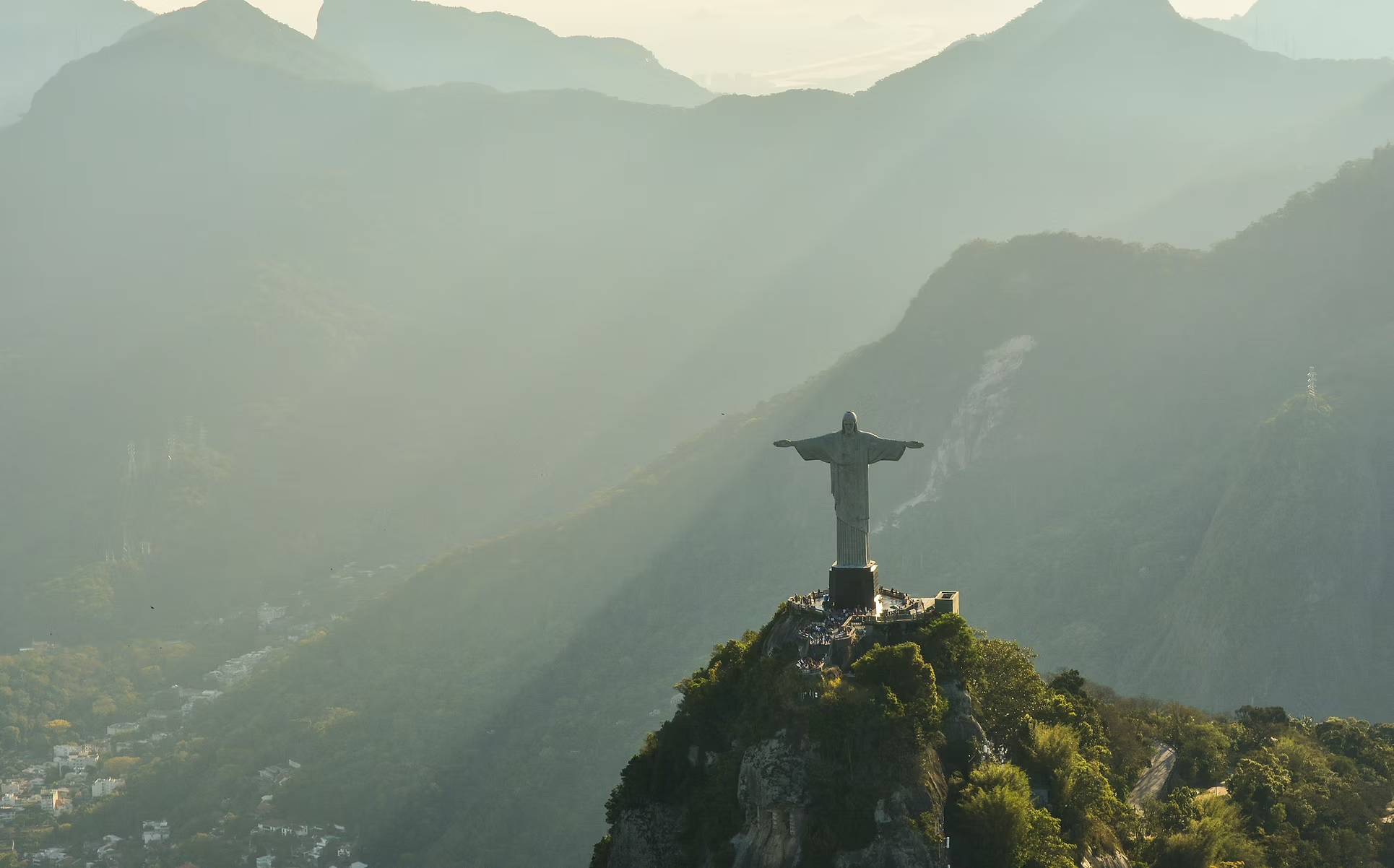Vue aérienne de la statue du Christ Rédempteur surmontant la montagne à Rio de Janeiro, Brésil, avec des collines verdoyantes et une ville en contrebas, sous un ciel brumeux.