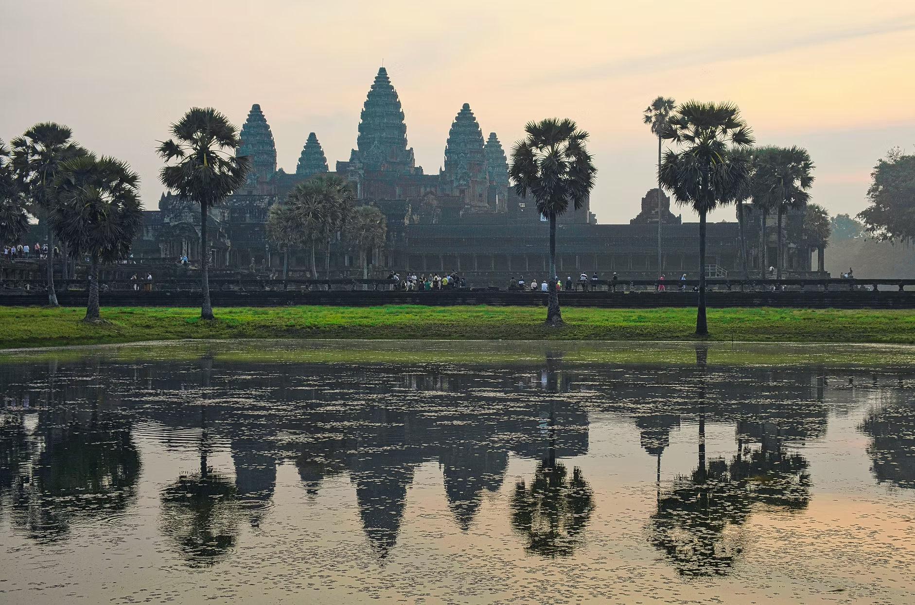 Le temple d'Angkor Vat au lever du soleil, entouré d'eau et de palmiers, avec des visiteurs explorant le site.