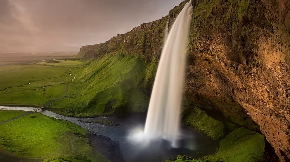 Cascade d'eau s'écoulant d'une falaise rocheuse sur un paysage verdoyant