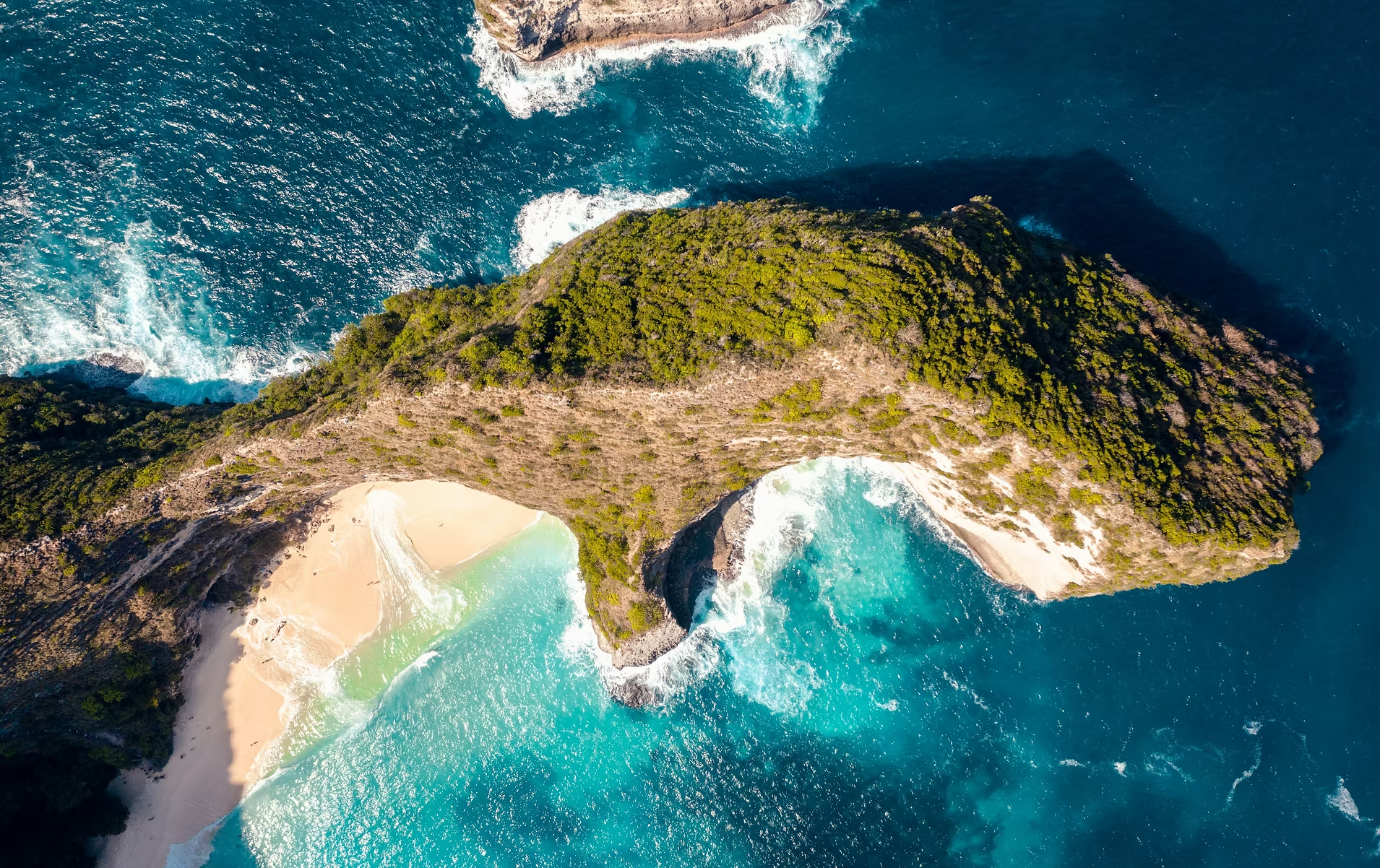 Vue aérienne d'une formation rocheuse en forme de pont naturel avec plages de sable blanc et eau turquoise.