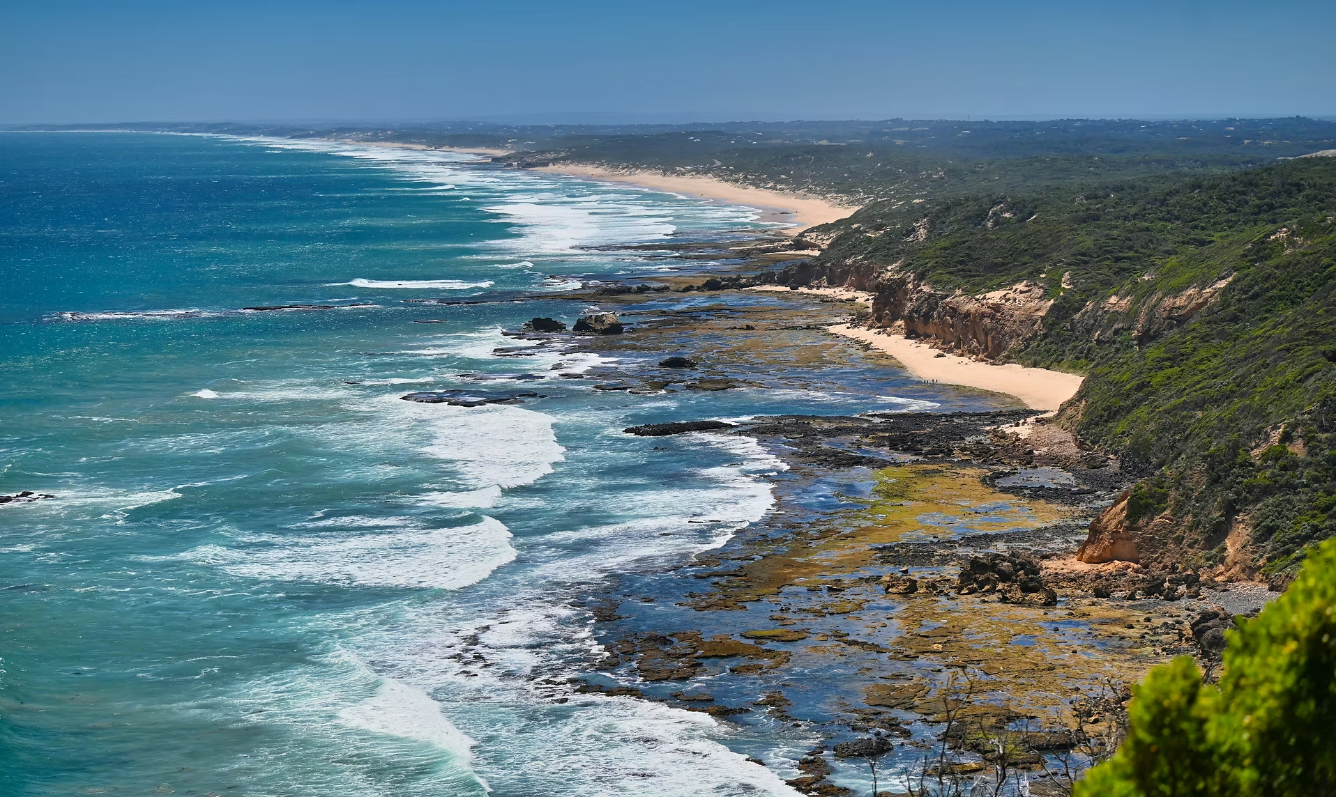 Côte rocheuse avec des falaises verdoyantes et une plage de sable vue depuis la montagne, océan Atlantique, ensoleillé.
