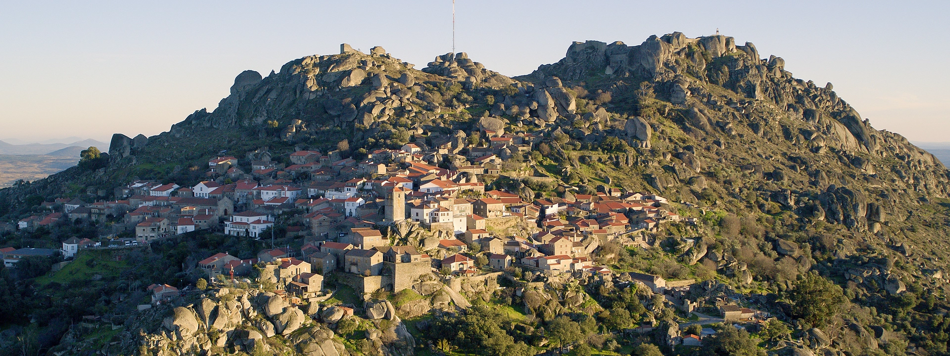 Petit village perchée sur une colline rocheuse, avec maisons aux toits rouges et une église au centre, entouré de rochers et de végétation