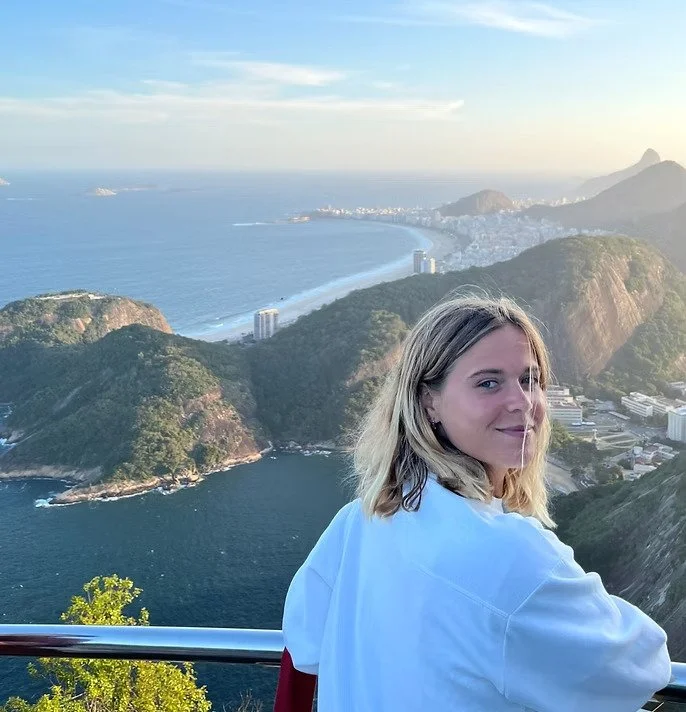 Une femme regarde la camera avec un fond de montagnes, mer et ville, au coucher du soleil.