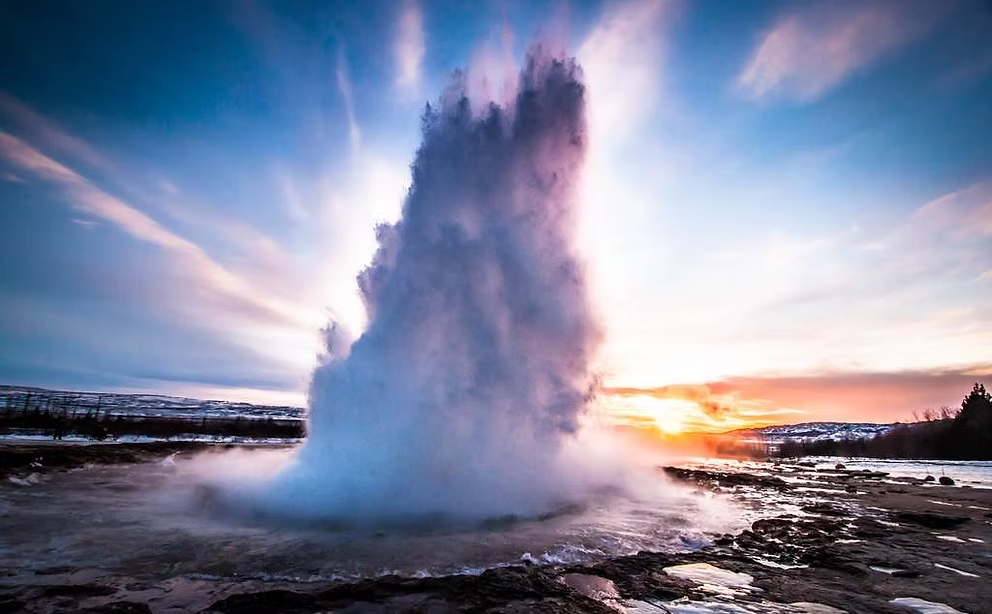 Éruption d'un geyser dans un paysage enneigé au coucher du soleil.