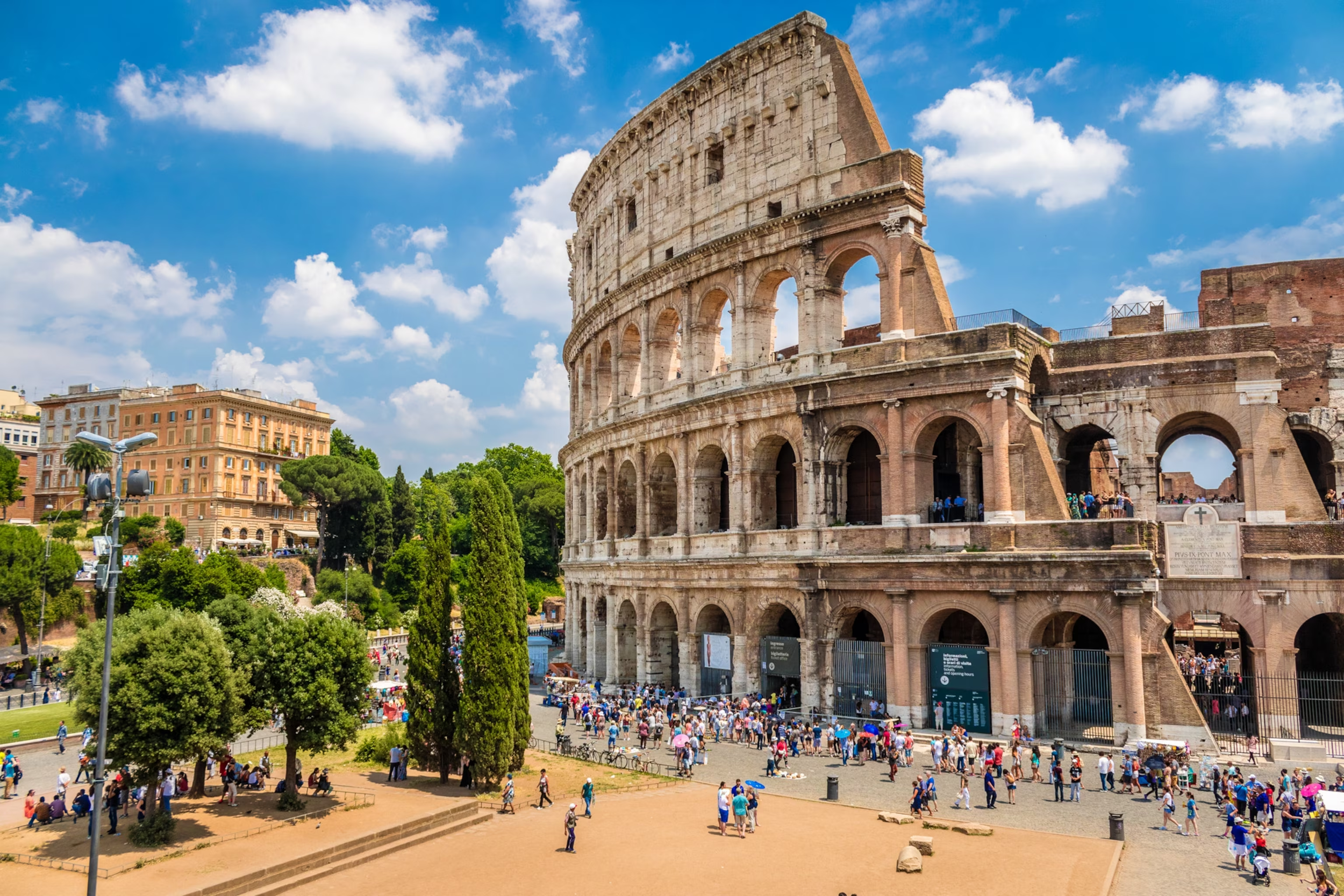 Le Colisée, amphithéâtre antique romain, vu en plein jour avec un ciel partiellement nuageux, entouré de touristes et de bâtiments modernes dans la ville de Rome.
