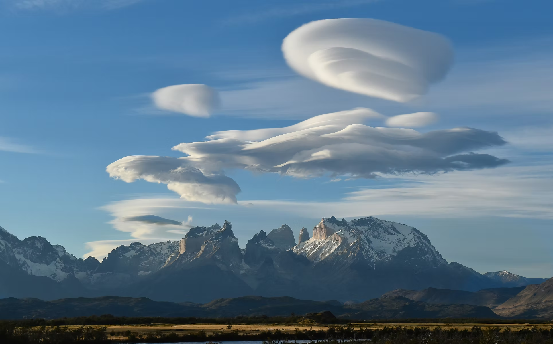 Montagnes enneigées sous un ciel bleu avec des formations nuageuses en forme de plaques et de spirales.