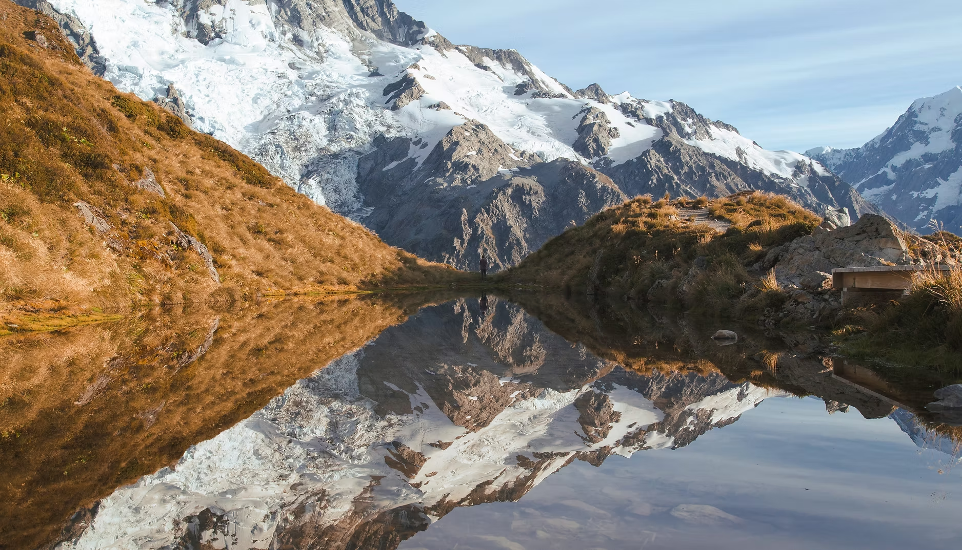 Paysage de montagne avec glacier enneigé, pentes rocheuses et reflet dans un lac calme