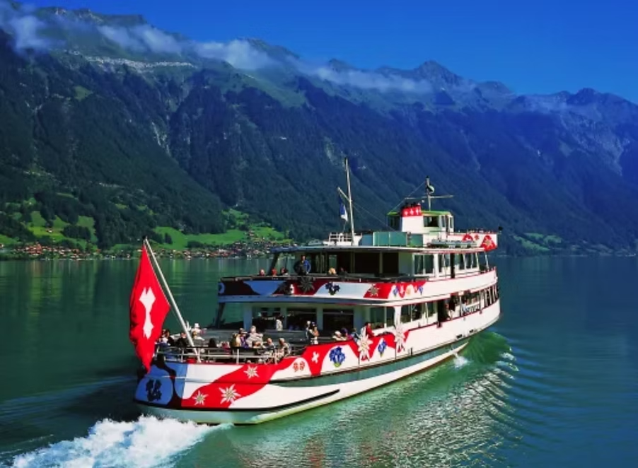 Un bateau naviguant sur un lac entouré de montagnes, décoré de motifs de Noël et d'une bannière rouge avec une croix blanche suisse.