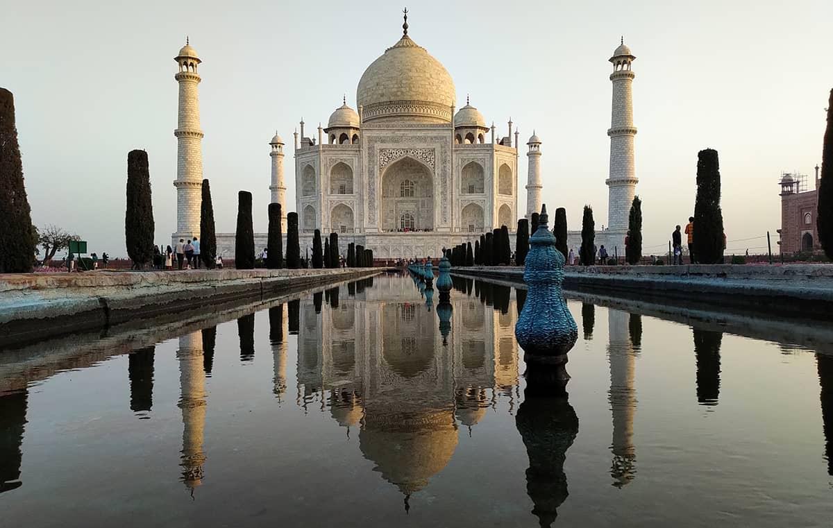 Le Taj Mahal vu depuis la piscine reflective avec des touristes et des arbres alignés.