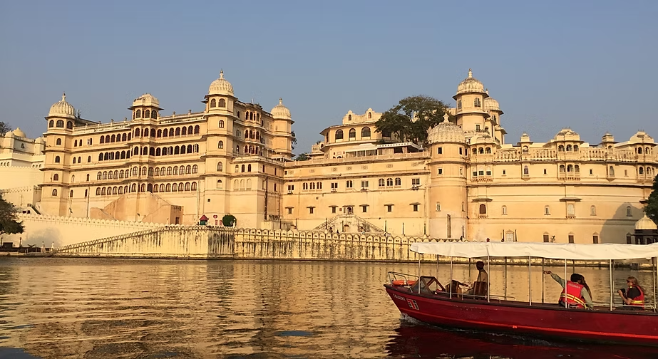 Un palais jaipur dans la ville indienne, vu depuis une rivière, avec un bateau rouge et des personnes à bord.
