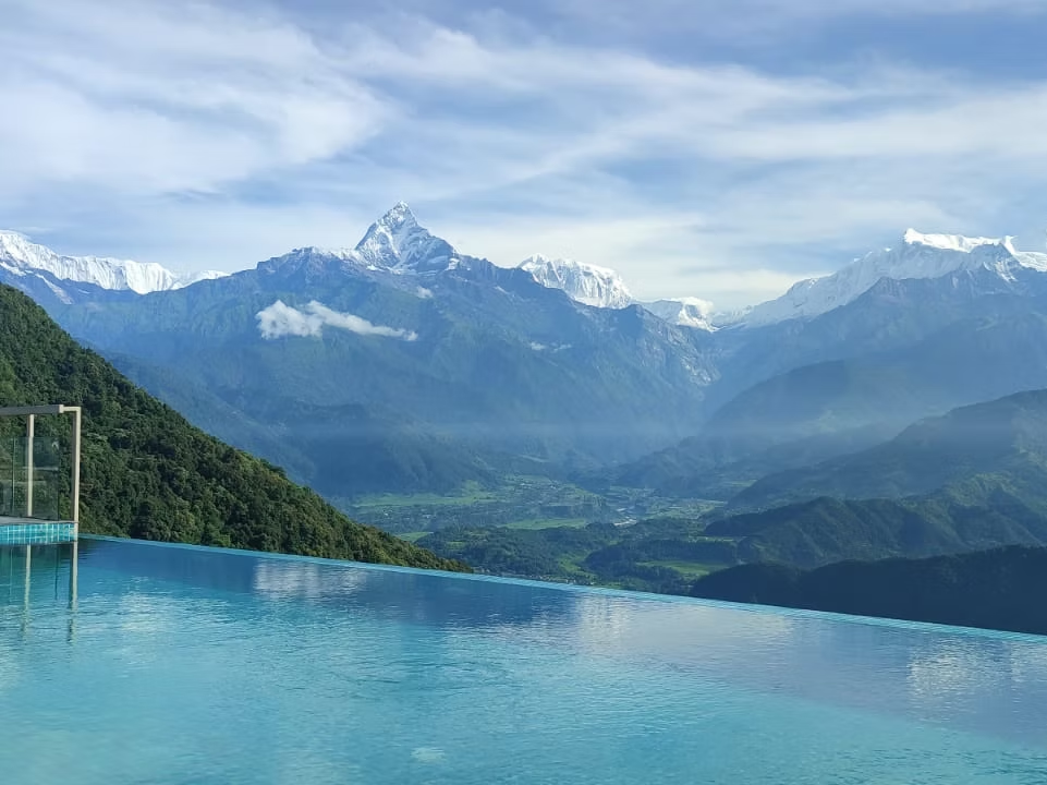 Vue de montagnes enneigées, vallée verdoyante et piscine à débordement avec vue sur la montagne.