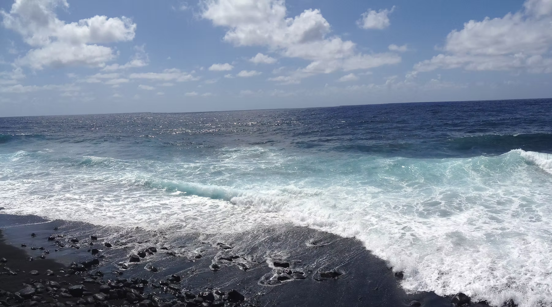 Vue d'une plage rocheuse avec des vagues de mer sous un ciel partiellement nuageux.
