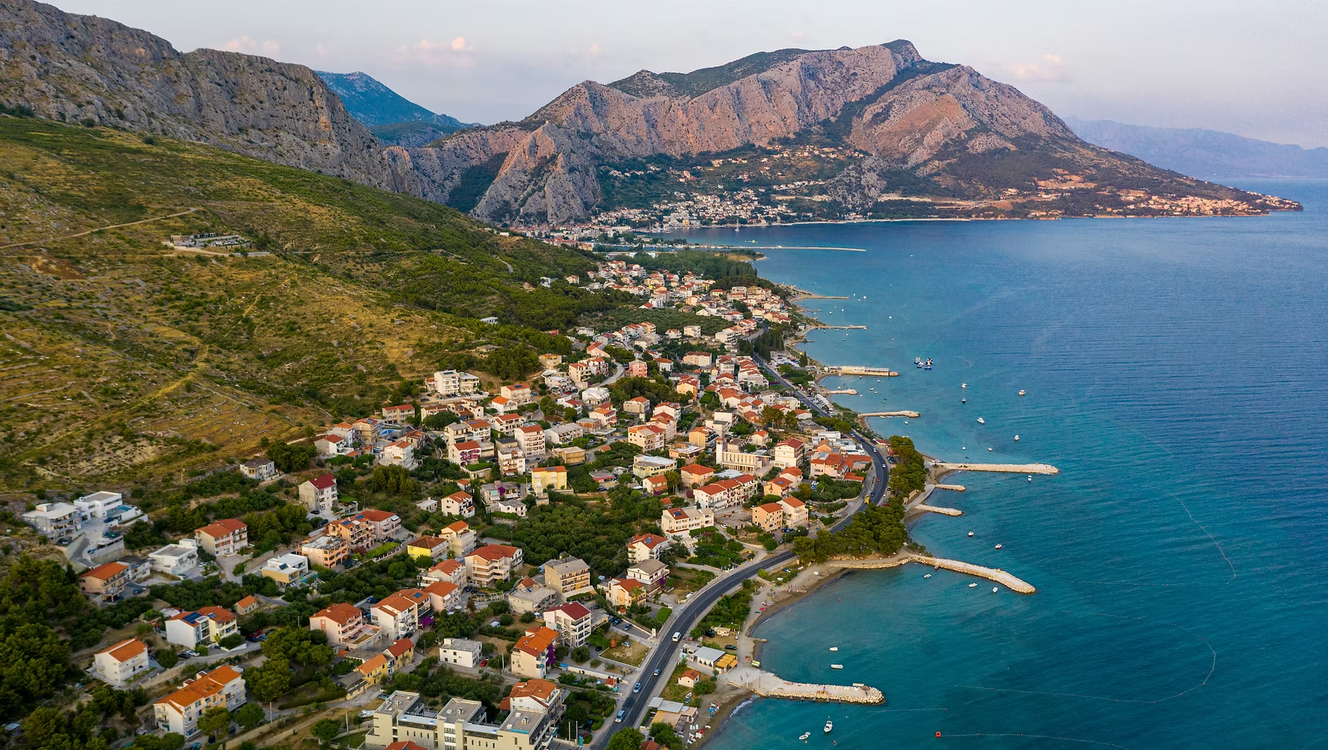 Une vue aérienne d'une ville côtière avec des bâtiments résidentiels et un littoral bordé de jetées, entourée de montagnes.