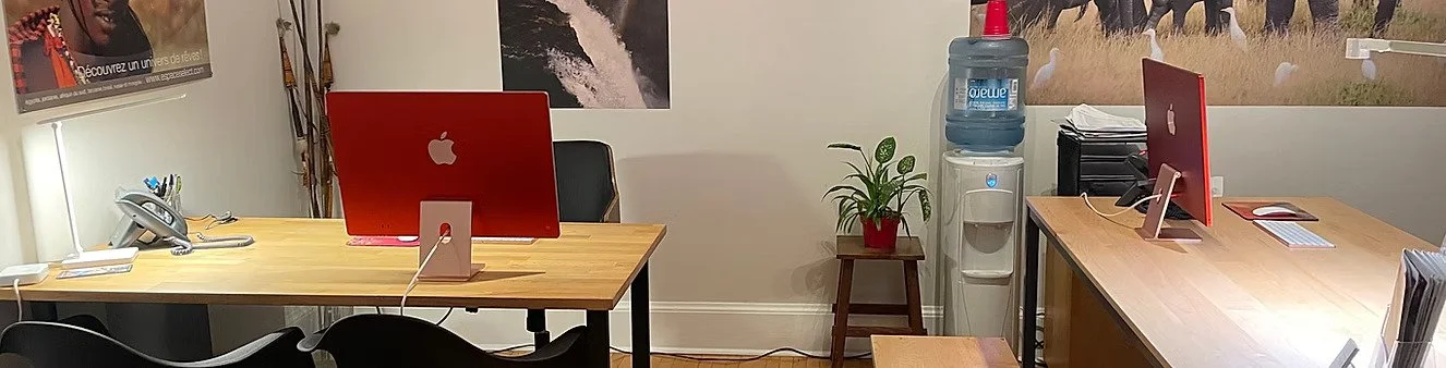 Bureau avec deux ordinateurs Apple, une plante en pot, un distributeur d'eau, et des posters sur le mur.