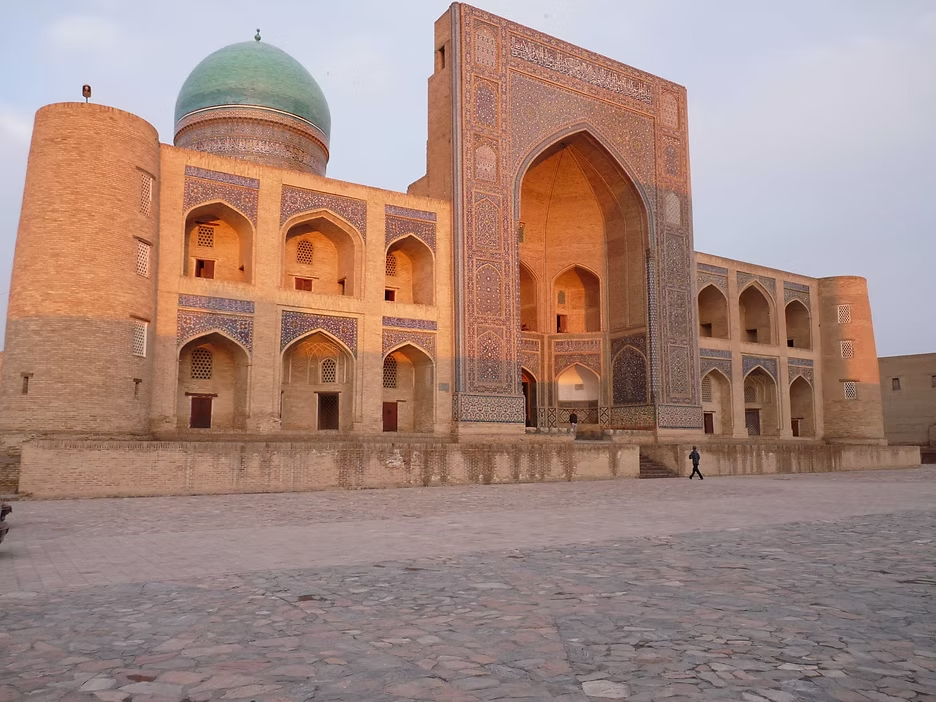 Un bâtiment historique en architecture islamique avec un grand portail orné de mosaïques colorées, une grande coupole verte et plusieurs fenêtres en arches.