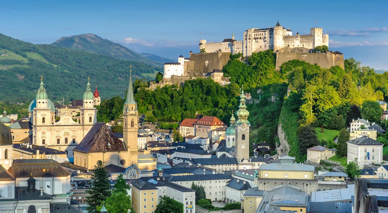 Vue panoramique de la vieille ville d'Innsbruck avec la cathédrale, les églises, et le château sur la colline entourés de montagnes verdoyantes sous un ciel bleu