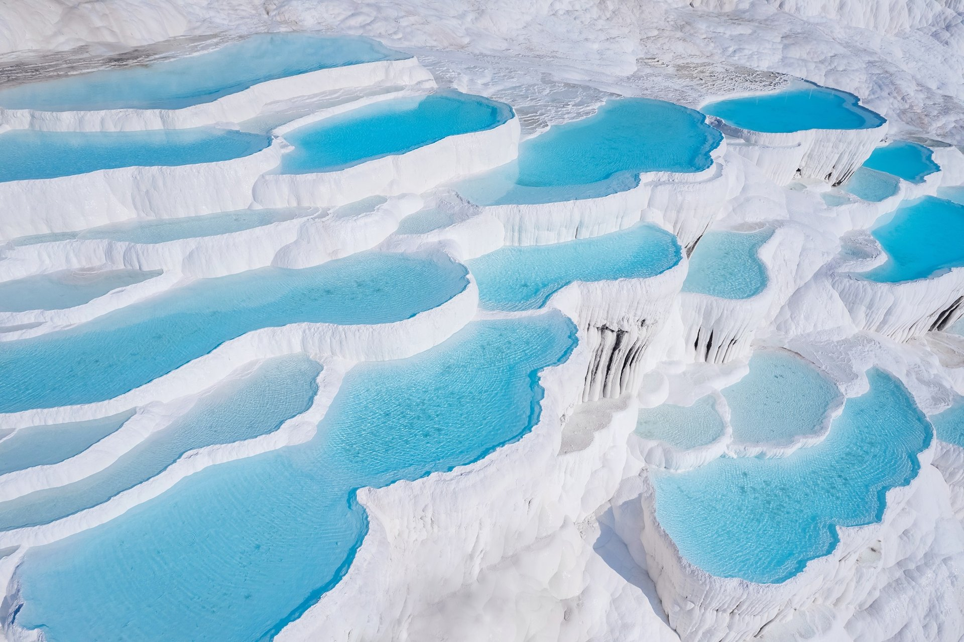 Lacs de turquoise sur une formation de marbre blanc en terrasses, formant une scène glacée et spectaculaire.