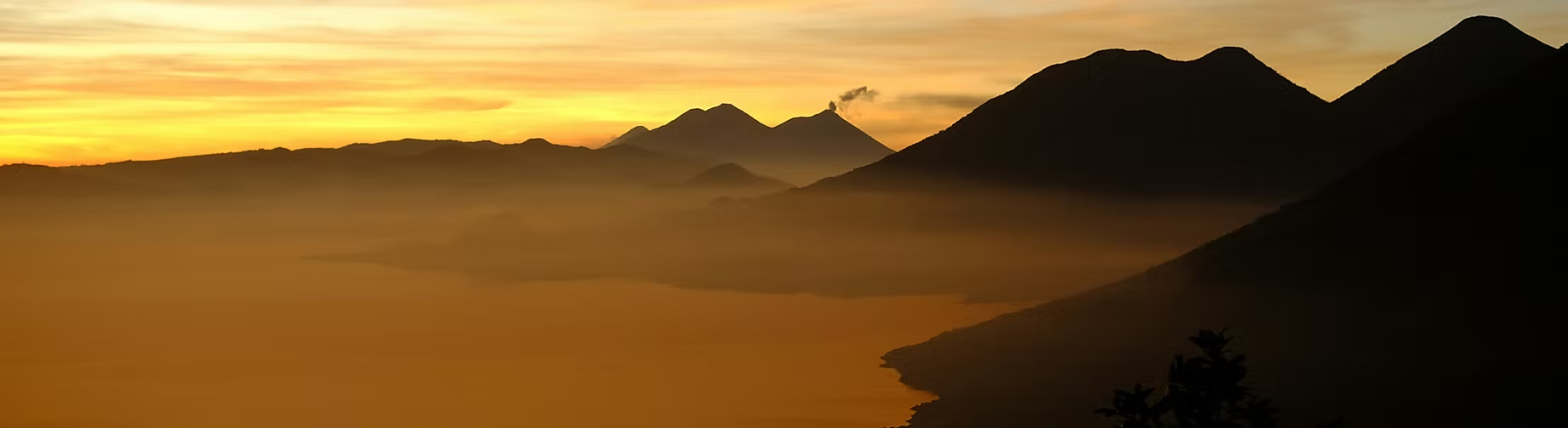 Coucher de soleil sur des montagnes sombres avec des nuages et de la brume au premier plan.