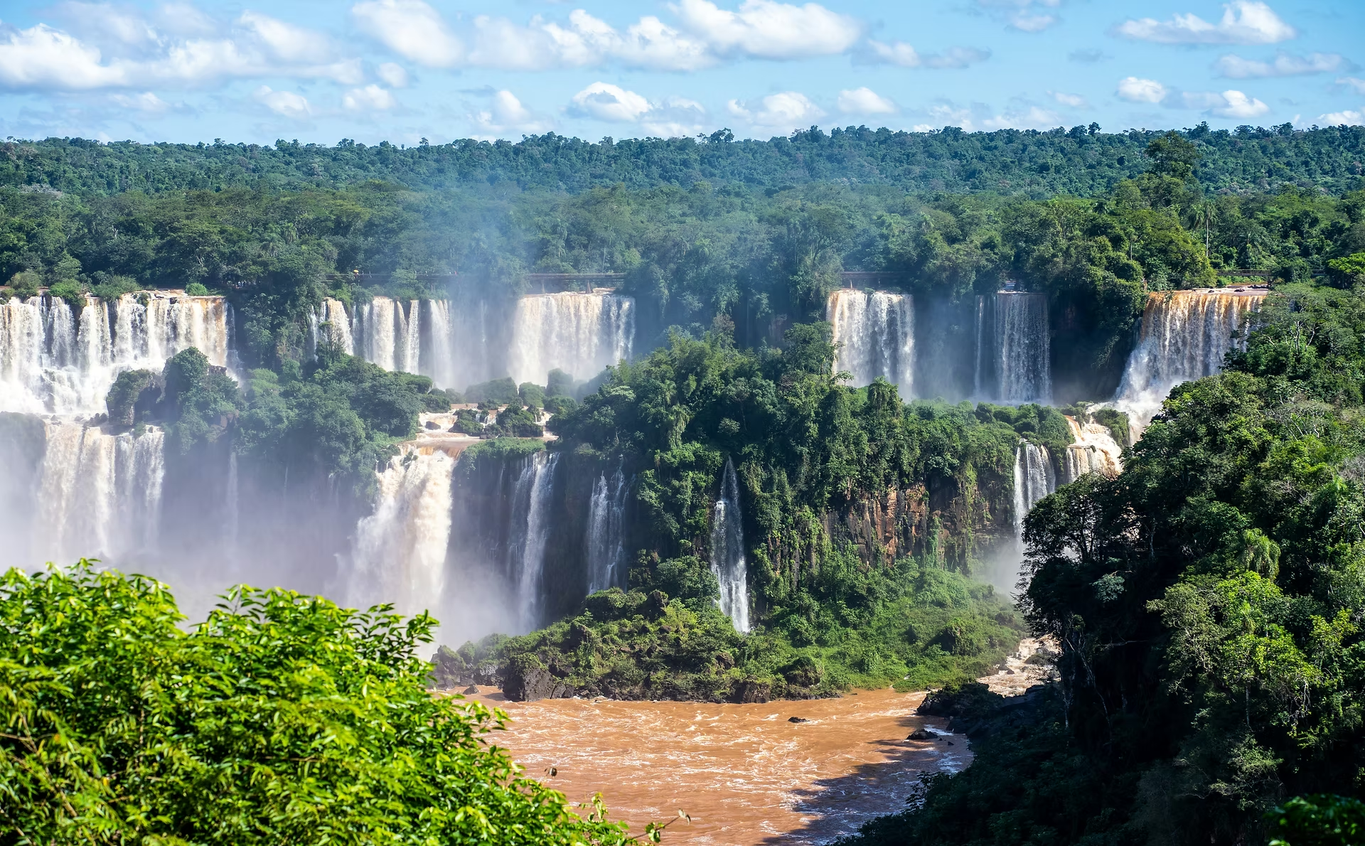 Chutes d'eau puissantes entourées de forêt tropicale verte, sous un ciel partiellement nuageux.