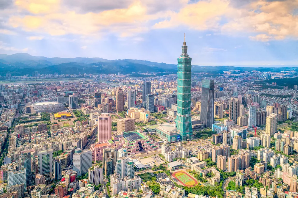 Vue aérienne de Taipei, avec la tour Taipei 101 centrale et de nombreux bâtiments environnants, sous un ciel partiellement nuageux.
