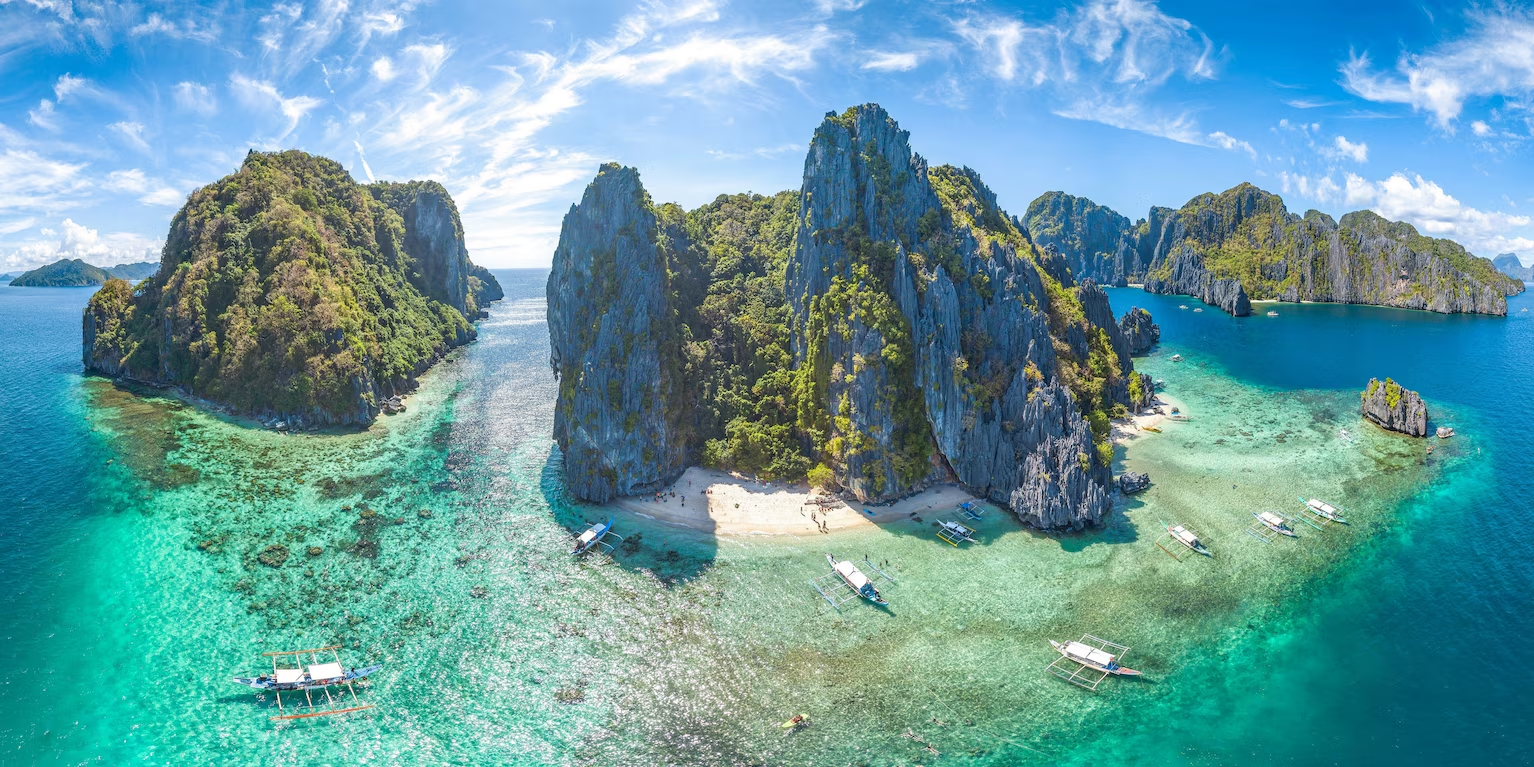 Paysage d'îles rocheuses avec eau turquoise, plages, et bateaux traditionnels en Indonésie