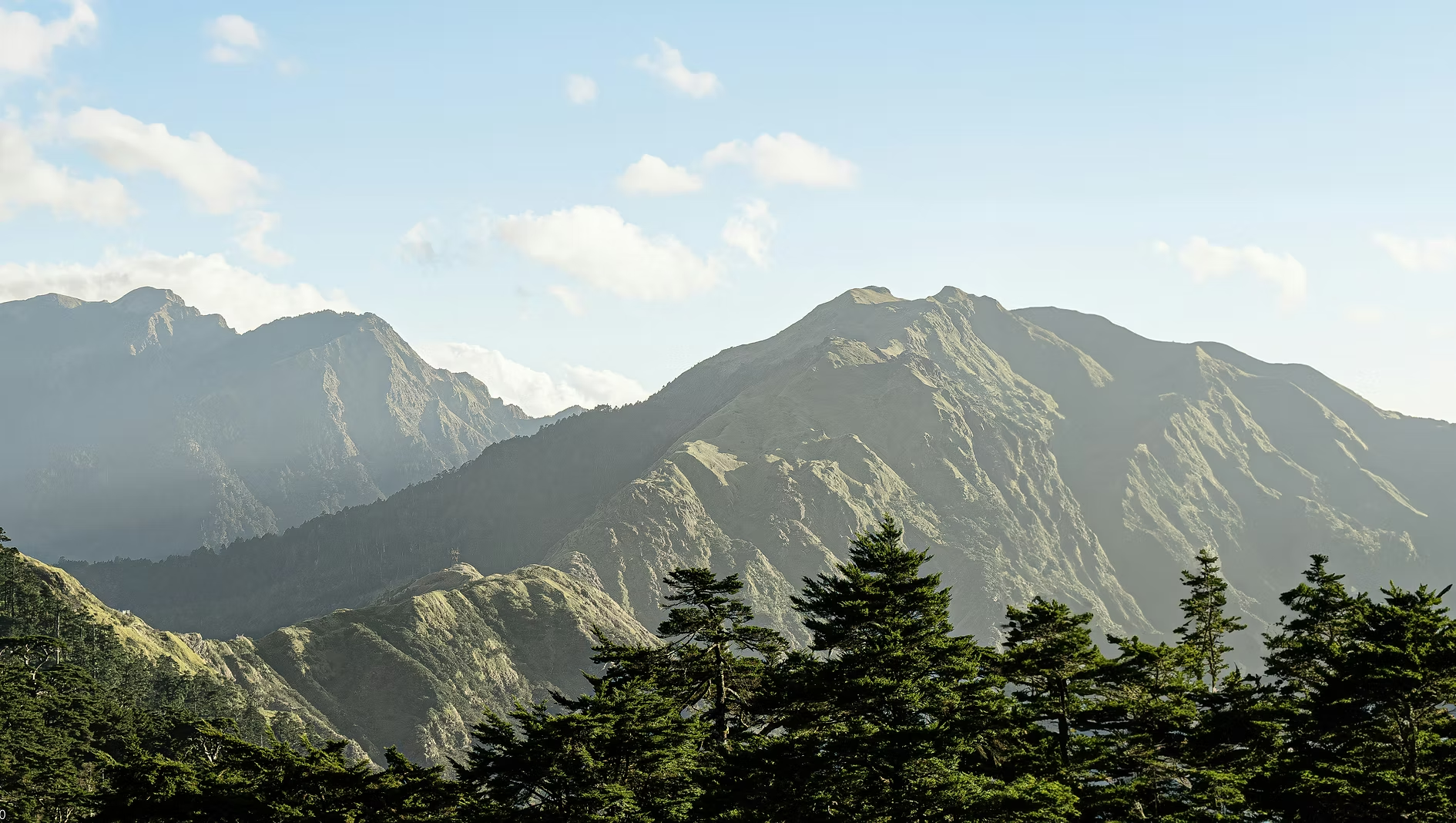 Montagnes verdoyantes sous un ciel bleu avec quelques nuages.
