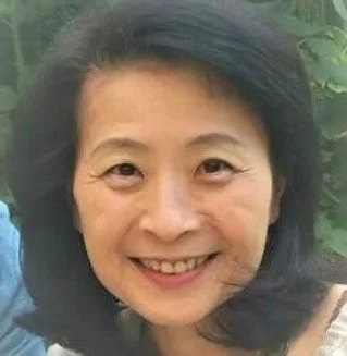 Portrait d'une femme souriante avec des cheveux noirs et un fond de nature verdoyante.