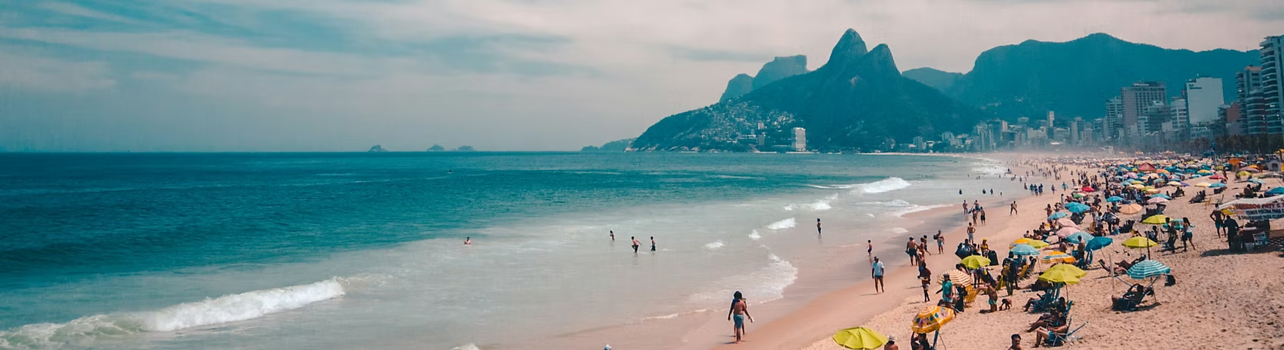 Plage animée avec de nombreux parasols colorés, des gens qui se baignent et se relaxing, et des montagnes en arrière-plan.