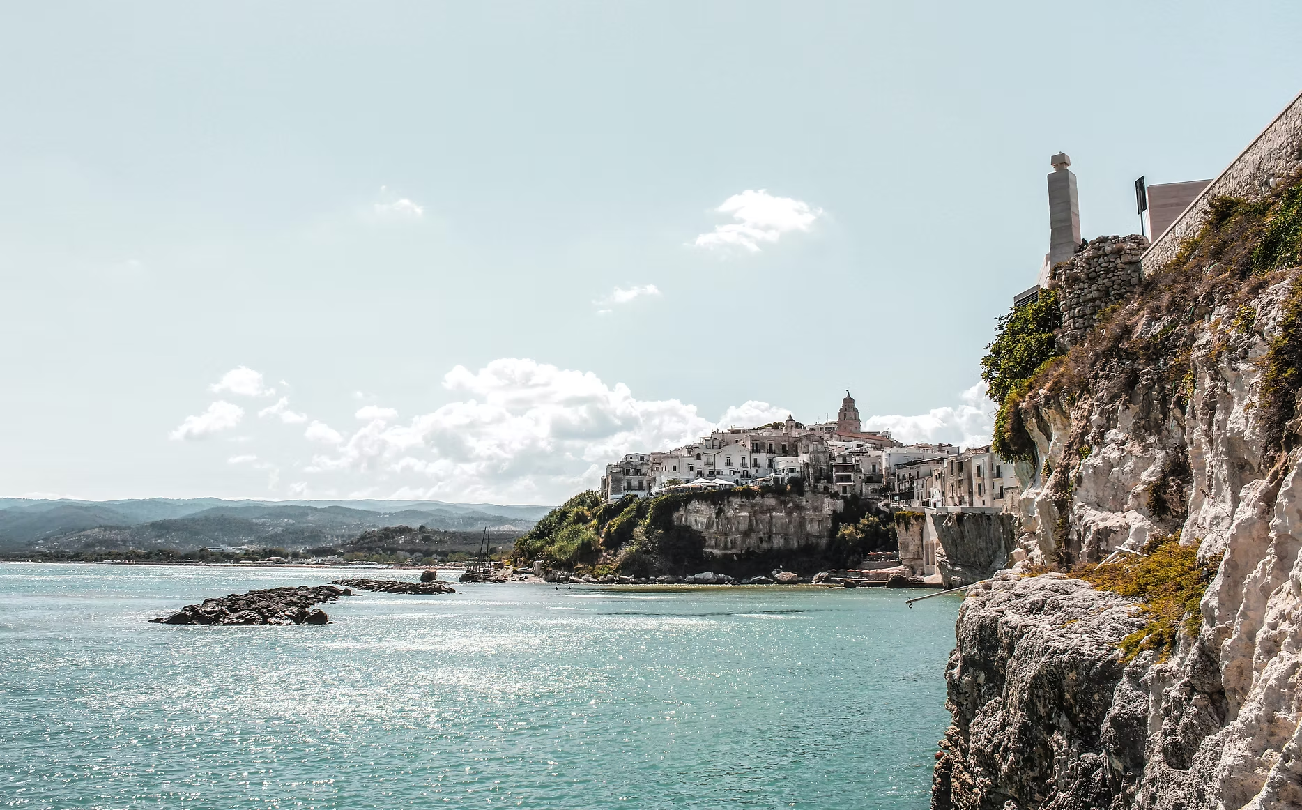 Paysage côtier avec une falaise rocheuse, un village blanc sur la colline, et la mer au premier plan.