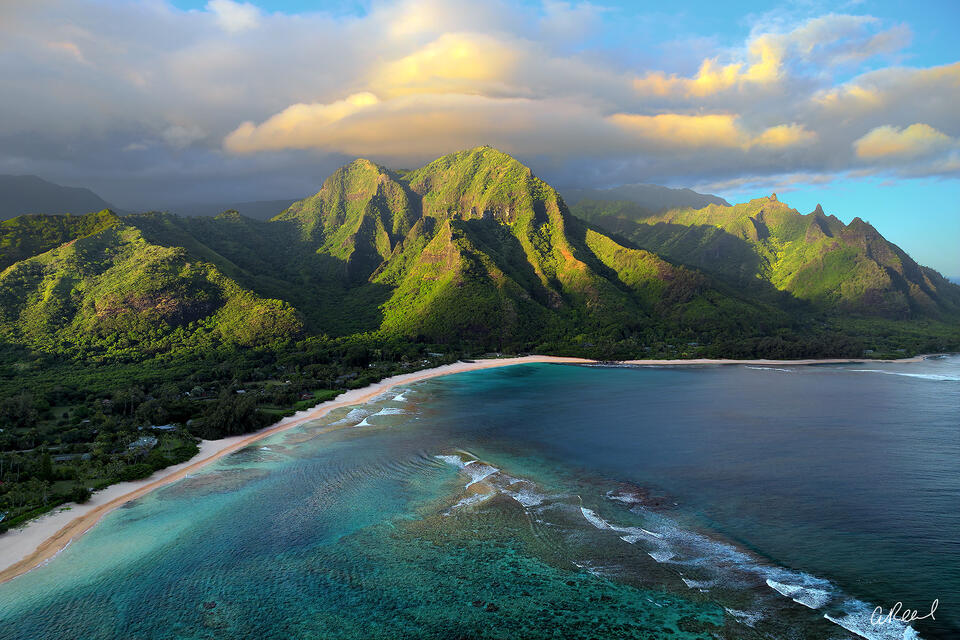 Paysage côtier avec des montagnes vertes, une plage de sable blanc et une mer turquoise.