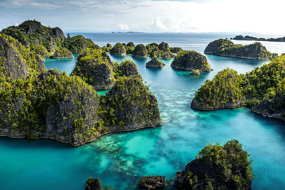 Criques tropicales avec eaux turquoise entre des îles couvertes de végétation dense, sous un ciel partiellement nuageux.