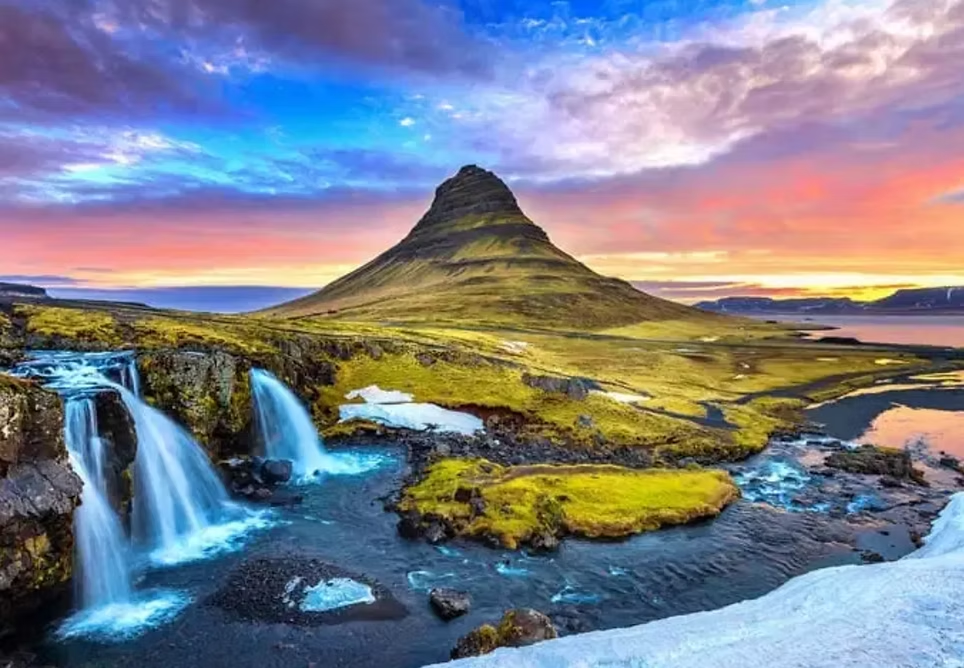 Un paysage de montagne avec une cascade, une rivière et un sommet en forme de pyramide, sous un ciel coloré lors du coucher du soleil.