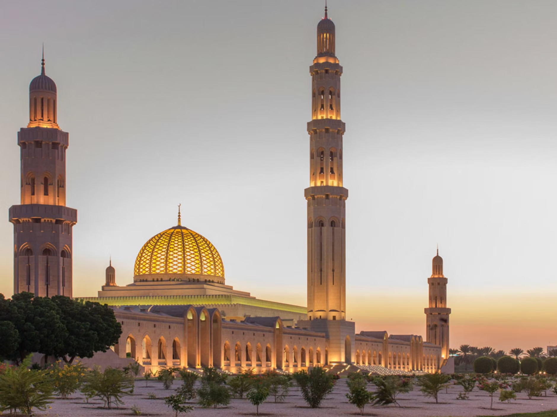 Une mosquée illuminée au coucher du soleil avec un dôme doré et plusieurs minarets.
