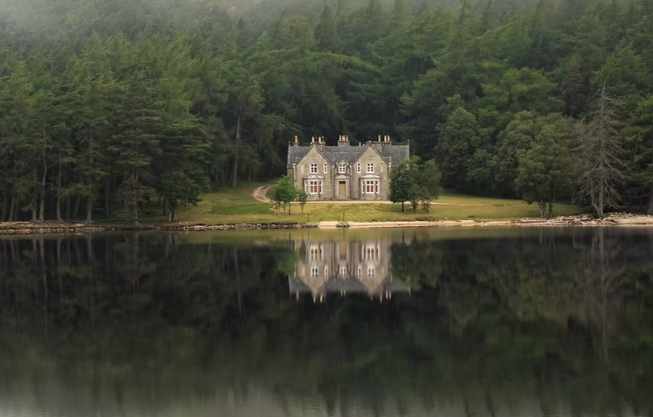 Un château en pierre au bord d'un lac calme, entouré d'une forêt dense.