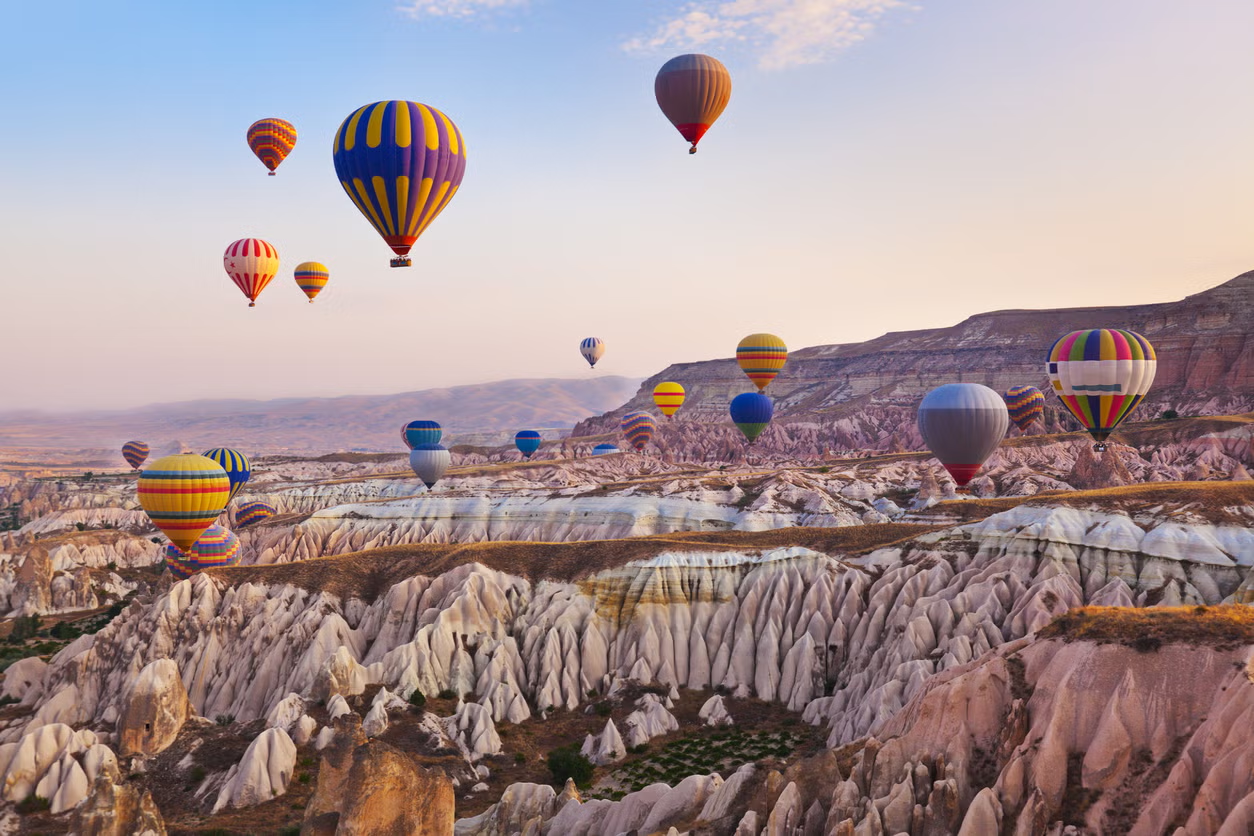 Montgolfières colorées flottant au-dessus d'un paysage rocheux de Cappadoce au lever ou coucher du soleil.