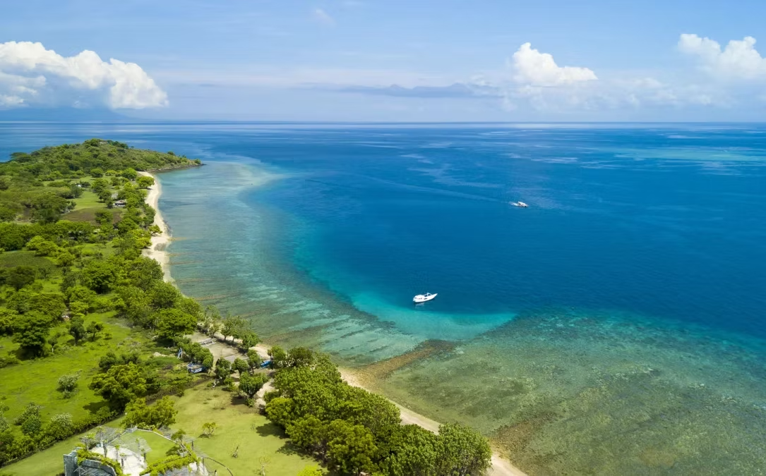 Côte tropicale avec plage, végétation luxuriante, eaux turquoise et deux bateaux à l'horizon.