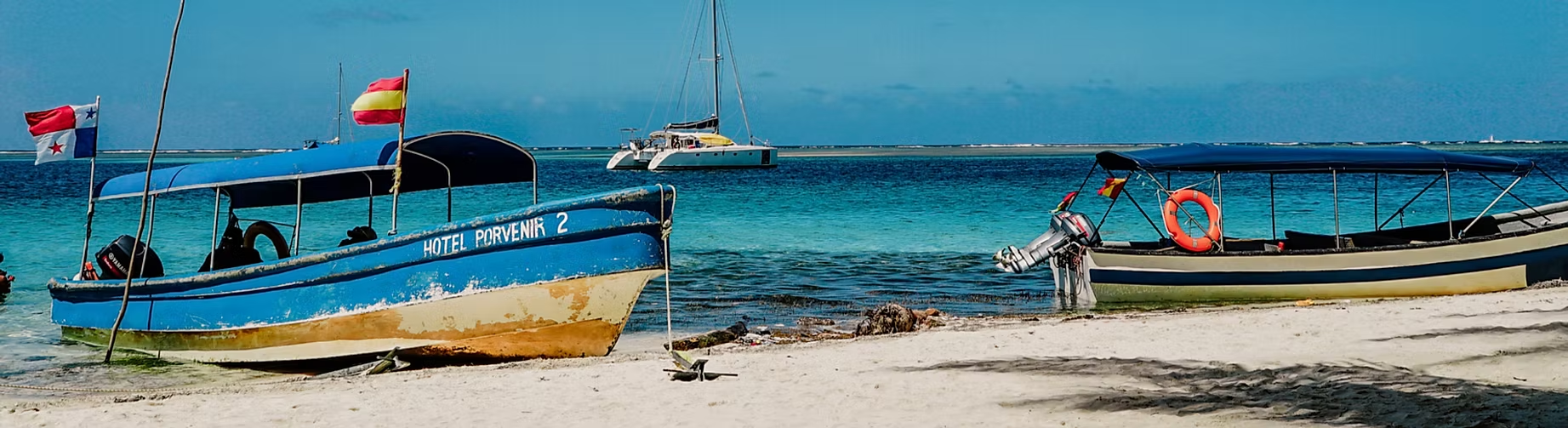 Deux bateaux à moteur sur la plage, avec la mer en arrière-plan, un bateau en bas à gauche et un autre à droite, les deux avec des drapeaux, un drapeau panaméen et un drapeau national espagnol.