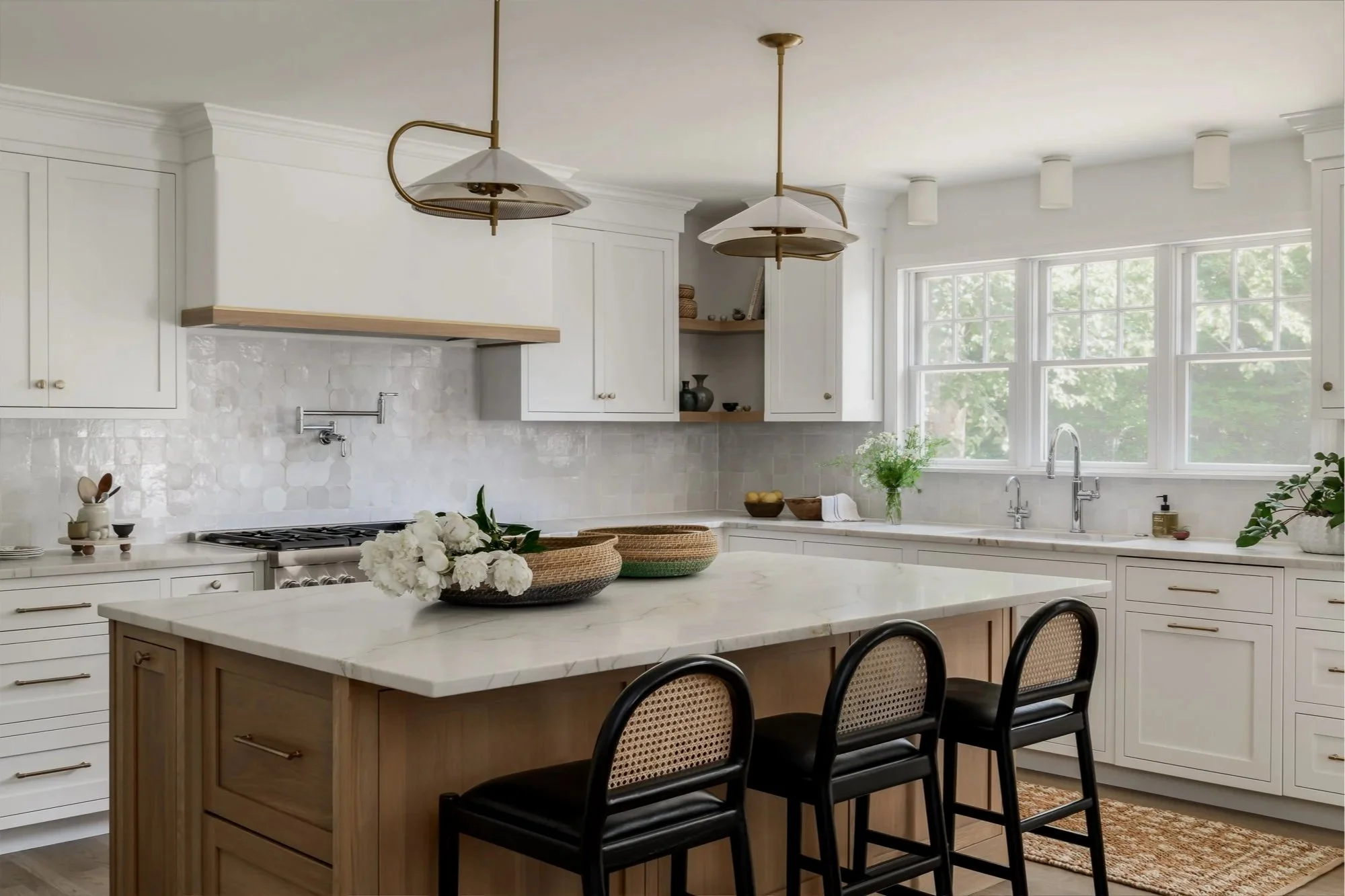 Bright, modern kitchen with white cabinets, a large marble island, a window view of green trees, and decorative plants and bowls on the counters.