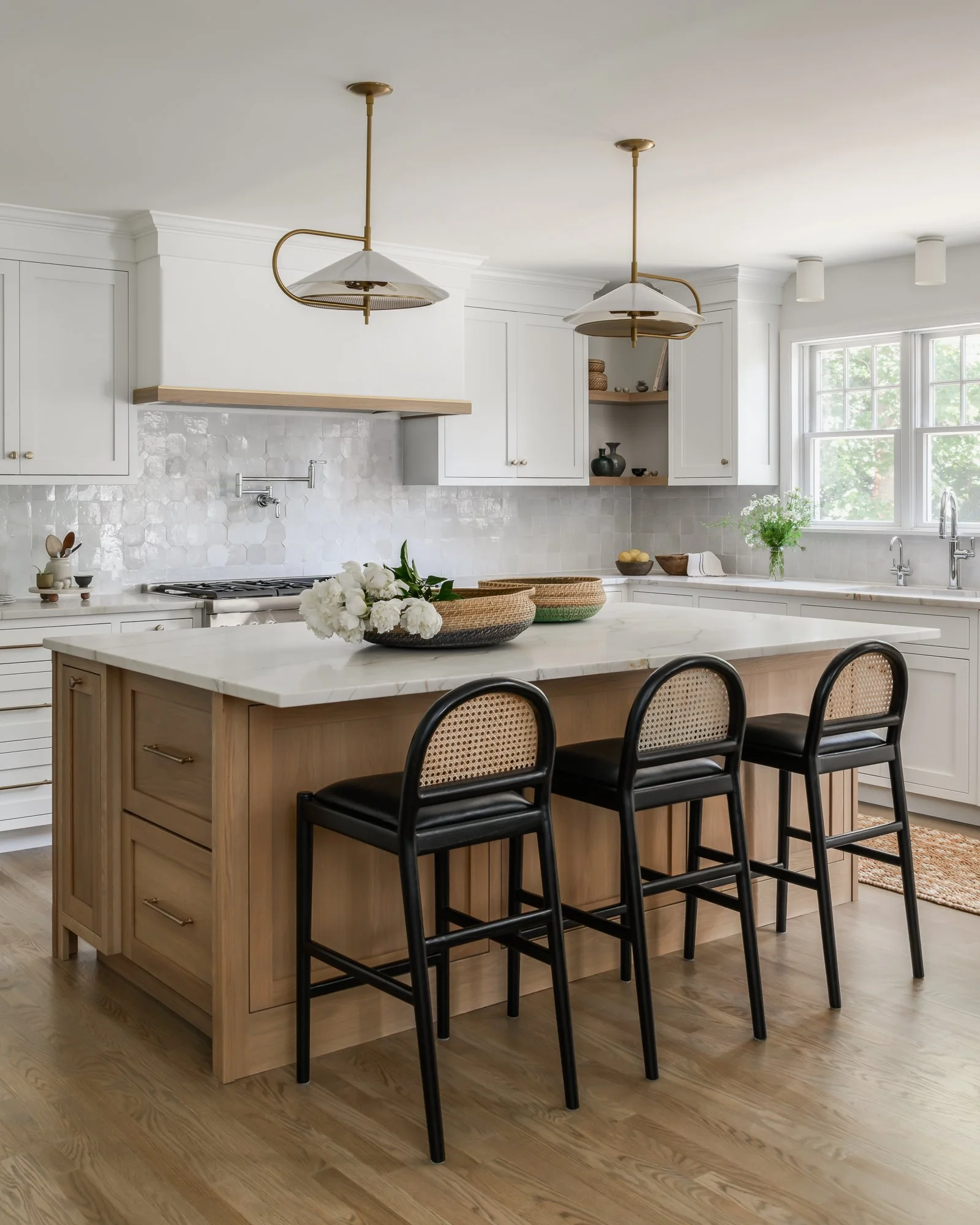 Modern kitchen with white cabinets, a white marble island, black bar stools, and decorative items including bowls, vases, and flowers.
