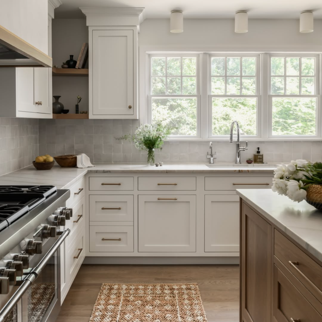 Kitchen with white cabinets, a marble countertop, a window above the sink, and a wooden kitchen island with a vase of white flowers.