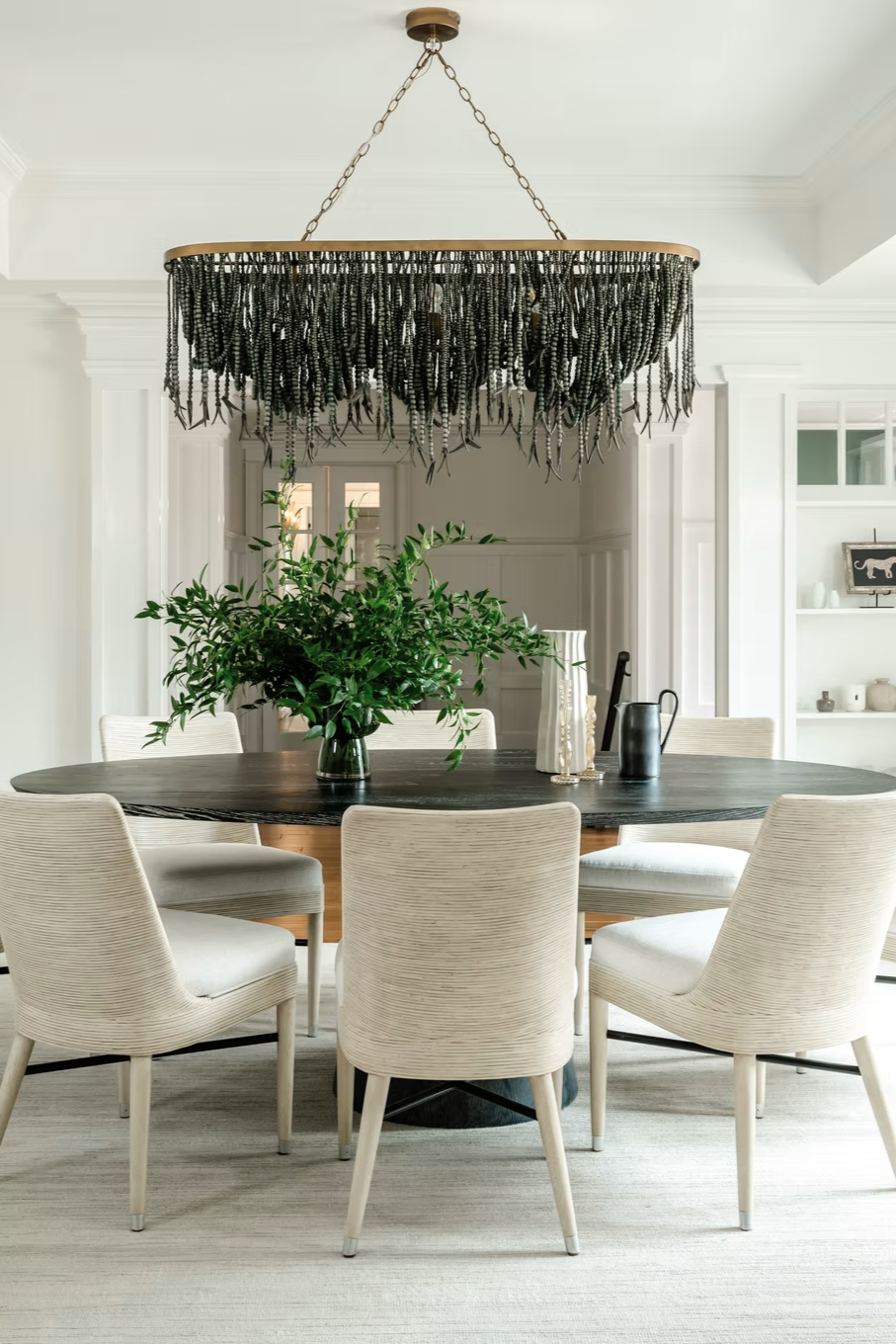Bright renovated dining room with an oval wood table, upholstered chairs, and black beaded chandelier