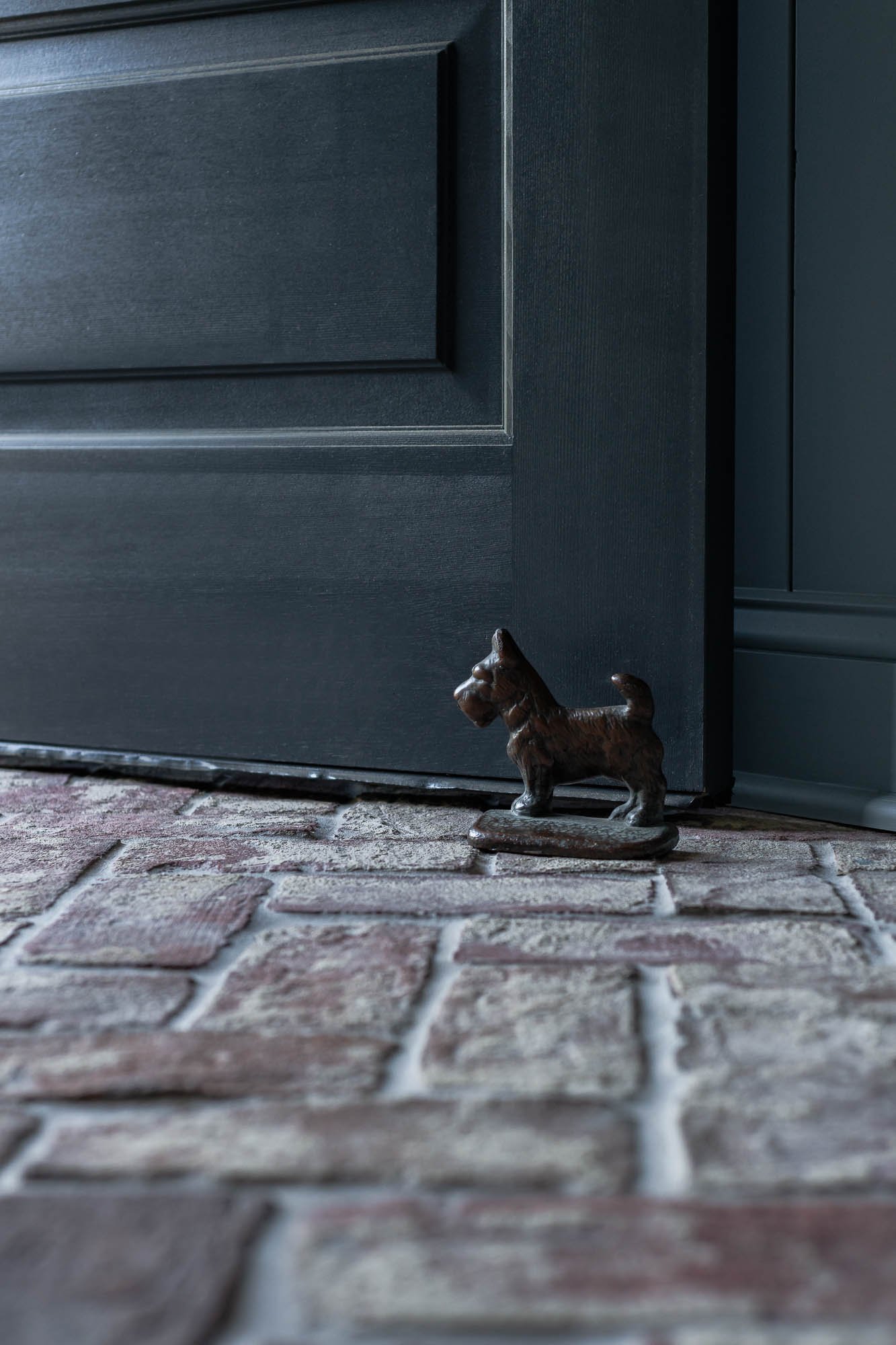 Small bronze or metal cat sculpture on a brick porch, in front of a dark gray door.