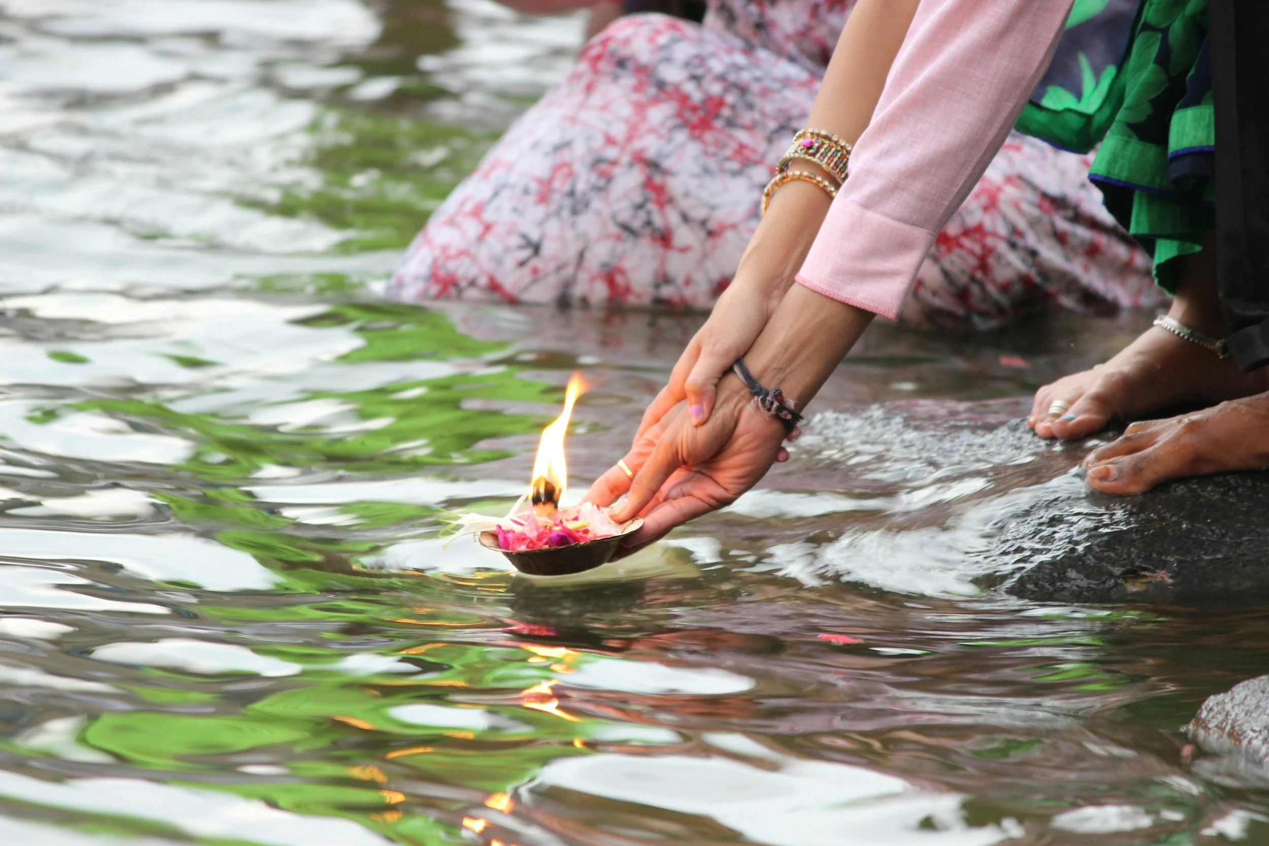 Menschen, die bei einem religiösen Ritual, vermutlich Katharsis, im Wasser eine kleine brennende Kerze in einer Schale mit Blumen halten.