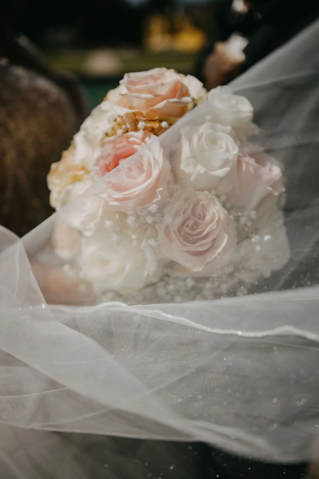 Ein Brautstrauß mit rosa und weißen Rosen, eingewickelt in Tüllstoff.