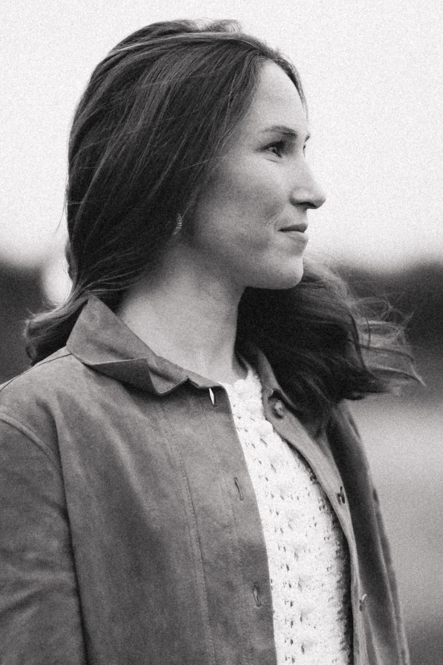 Black and white photo of a woman with long hair, wearing a light-colored sweater and a darker jacket, looking to the right.