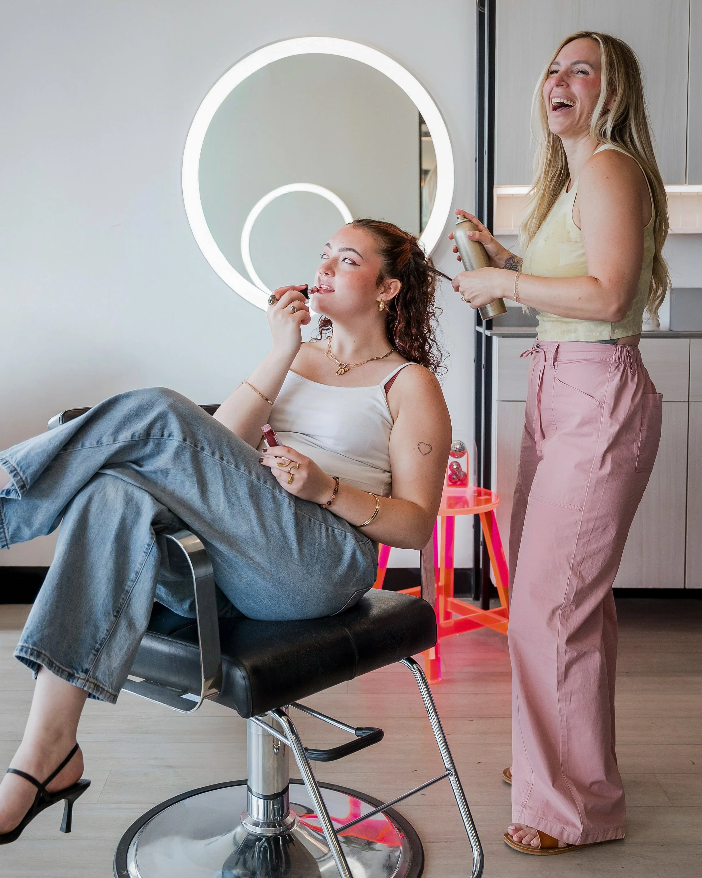 A NJ based blonde and extension specialist hairstylist laughing with her happy client.