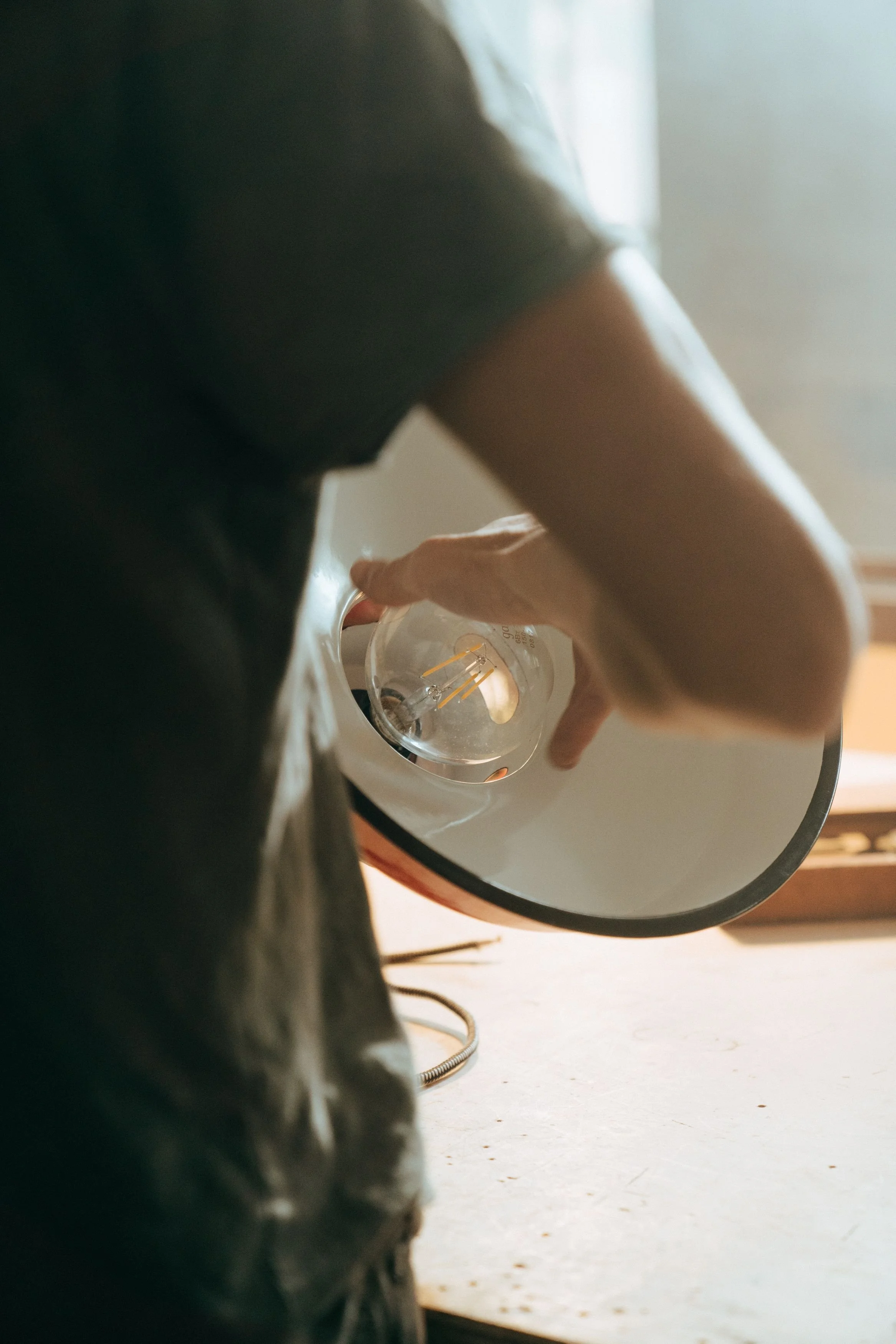 Person adjusting a lightbulb in a ceiling lamp. The photo is taken from a low angle, with part of the person's arm and shoulder visible.
